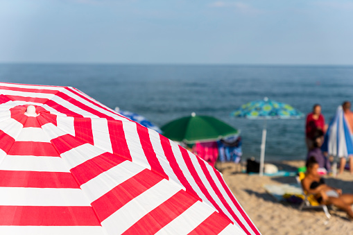 Striped beach umbrella at the beach with tourists and sea in background