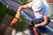 Worker building photovoltaic solar panel system on rooftop of house with help of hex key.
