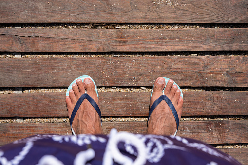 Mans feet in flip flops on wooden boardwalk. Top view. Flat lay. Empty space, for text or logo