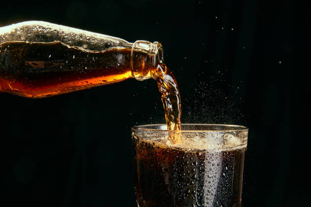 Soda, coke, dark beer pouring from bottle into glass against black background Soda, coke, dark beer pouring from bottle into glass against black background. Concept of alcohol and non-alcohol drinks, refreshment. Poster, banner for ad coca cola stock pictures, royalty-free photos & images