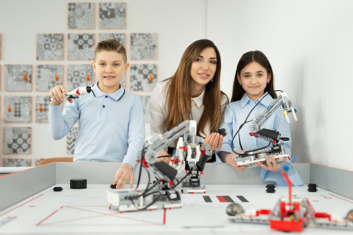 Young beautiful mother with her son and daughter pose at the school of robotics with robots from the constructor.