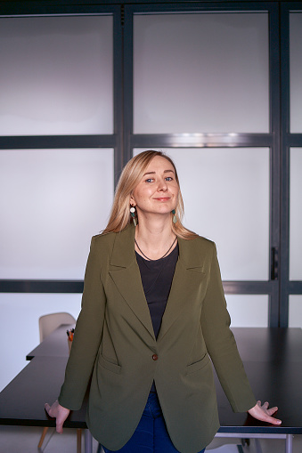 blonde woman with long hair in a green jacket and jeans in the office