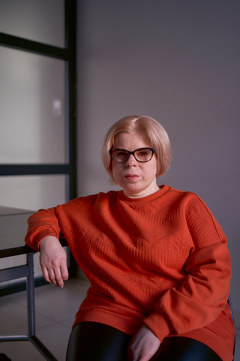portrait of a woman with a disability in an orange sweater and leather pants in the office