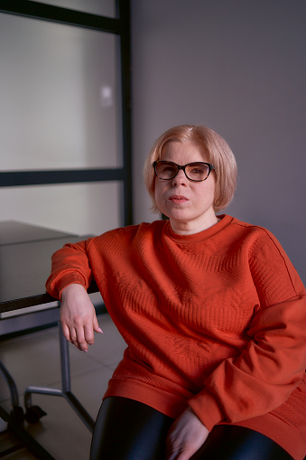 portrait of a woman with a disability in an orange sweater and leather pants in the office