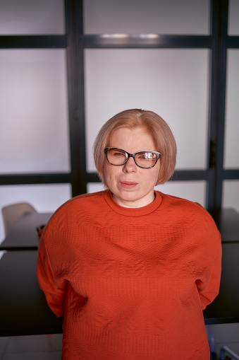 portrait of a woman with a disability in an orange sweater and leather pants in the office