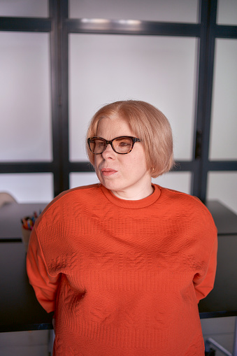 portrait of a woman with a disability in an orange sweater and leather pants in the office