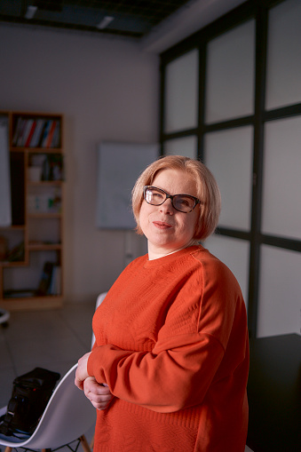 portrait of a woman with a disability in an orange sweater and leather pants in the office