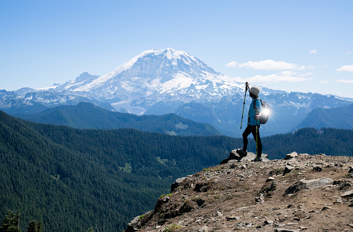Woman raising hiking pole towards Mount Rainier. Sunlight reflected on the metal drink bottle. Summit Lake trail. Mt Rainier National Park. Washington State.