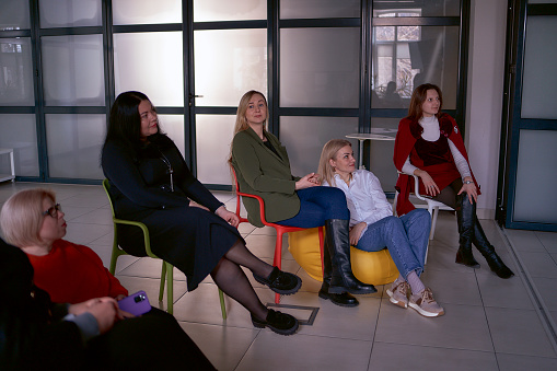 women watch their colleague's speach  on stage, sitting on chairs and Bean Bag