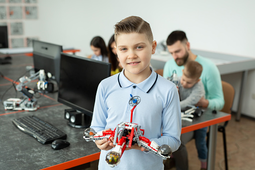 Portrait of a smart boy in a robotics class at school, holding a robot that he assembled from plastic parts programmed on a computer.