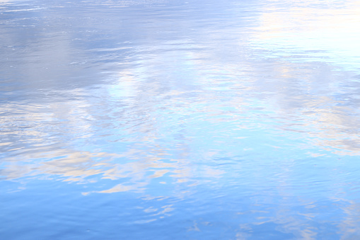 Reflection of clouds in water. The surface of water in a lake, river or flooded quarry. Ripples on the water. Beautiful color of water. Natural background