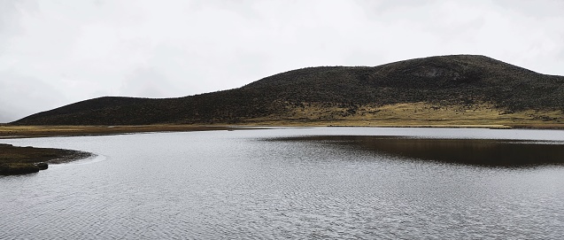A dark lake between cold hills against a cloudy sky
