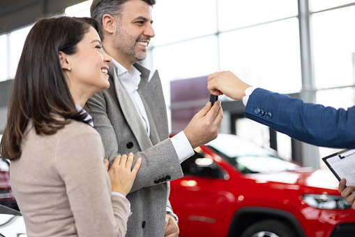 Car salesman giving car keys to excited couple in dealership setting