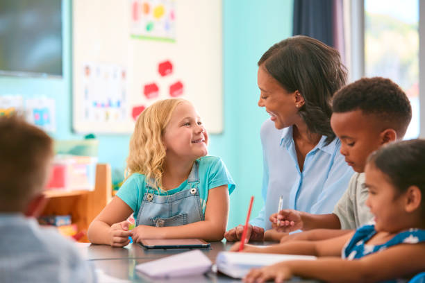 istock Female Primary Or Elementary School Teacher Helping Students With Digital Tablet At Table In Class 2098586675