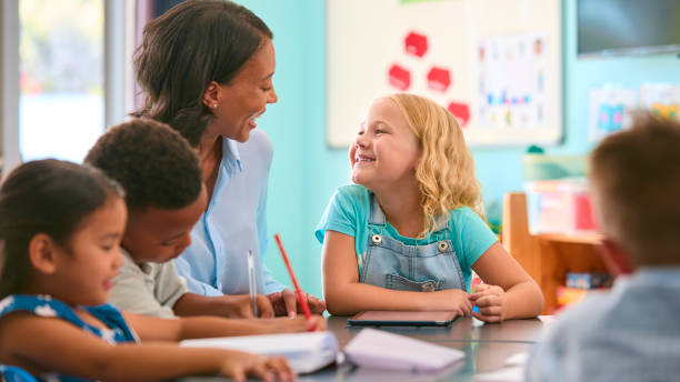 istock Female Primary Or Elementary School Teacher Helping Students At Desk In Multi-Cultural Class 2098590382
