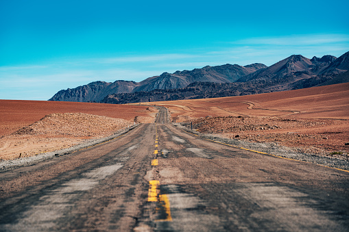 A deserted road stretches out in the vast Atacama Desert, surrounded by arid landscapes and blue skies in Chile.