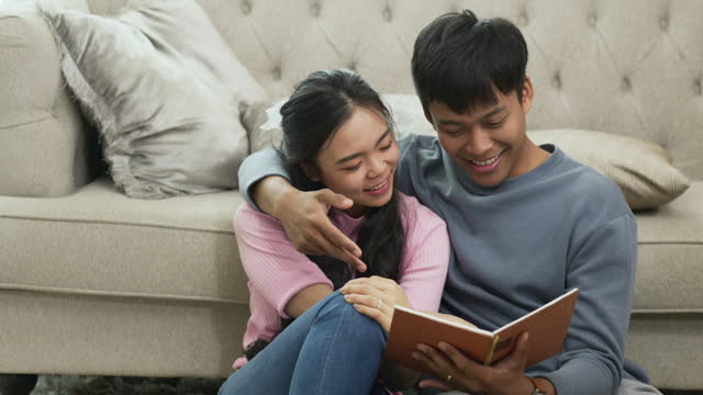 Slow motion shot relaxed young couple reading book on floor and spending weekend time together at home.