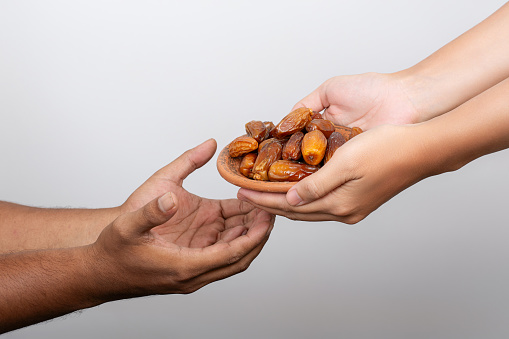 Hands sharing bowl of dates for ramadan iftar dinner. Ramadan kareem sharing food concept.