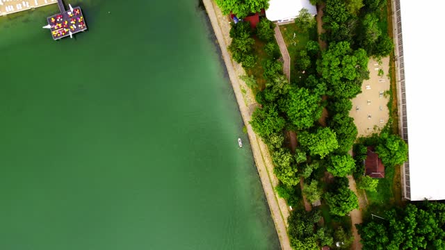 Top view of a lake with a white boat passing near the shore towards a pier