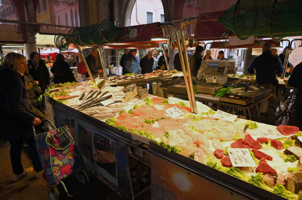 Venice, Italy, march 12, 2024 : Customers in front of a fish stall at the Rialto covered market in Venice