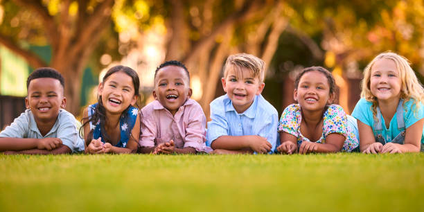 Portrait Of Multi-Cultural Primary Or Elementary School Student Friends Lying On Grass Outdoors
