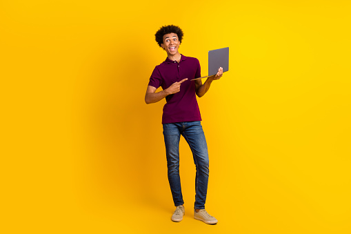 Full length photo of cheerful satisfied guy wear trendy purple polo recommend buy macbook isolated on yellow color background
