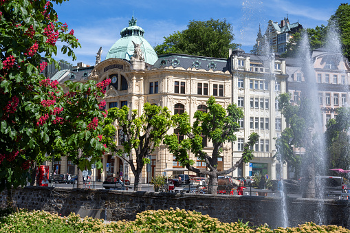 Karlovy Vary, Czech Republic -  June 3, 2023. Blossoming flowers, heritage buildings, and a fountain on a clear summer day.