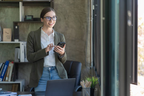 istock A happy young woman talking on her mobile phone and smiling while standing at her working place in the office. 2098661411