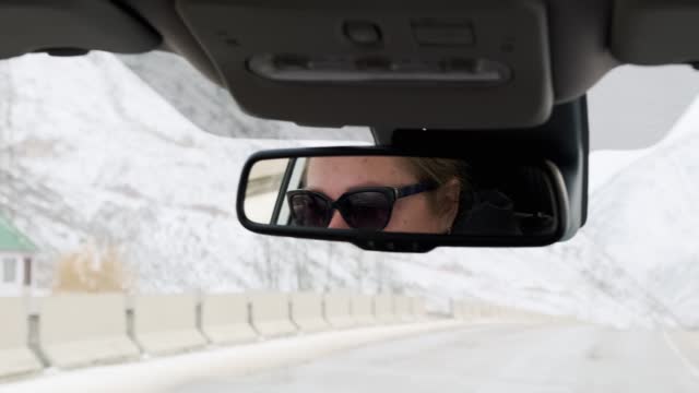 Woman driver driving a car in the rearview mirror, on an empty road covered snow, winter time