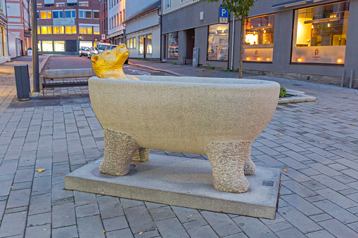 Sarpsborg, Norway - October 27, 2016: Sculpture of Golden Bear in Free Standing Bathtub at St. Marie Street Autumn Evening.