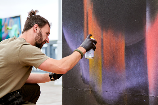 teenage boy spraying graffiti on a wall in park in Berlin