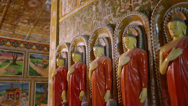 Line of Buddhist statues in ornate temple. Golden walls, intricate murals scenes. Robed figures stand serene, symbols of peace, meditation in spiritual sanctuary. Worship, culture blend sacred space.