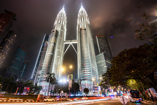 Kuala Lumpur,Malaysia-April 15 2023:The iconic KLCC Towers,the tallest twin skyscrapers in the world,light up the sky above with strong flood lighting,as streaks of light from vehicles rush by.