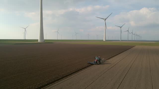 Aerial view of wind turbines and tractor plowing land, Flevoland, Netherlands
