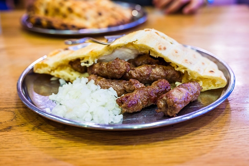 Traditional bosnian barbecue dish cevapi served with somun and chopped onions. Famous balkan BBQ dish served on an inox plate in Bascarsija, Sarajevo, Bosnia and Herzegovina.