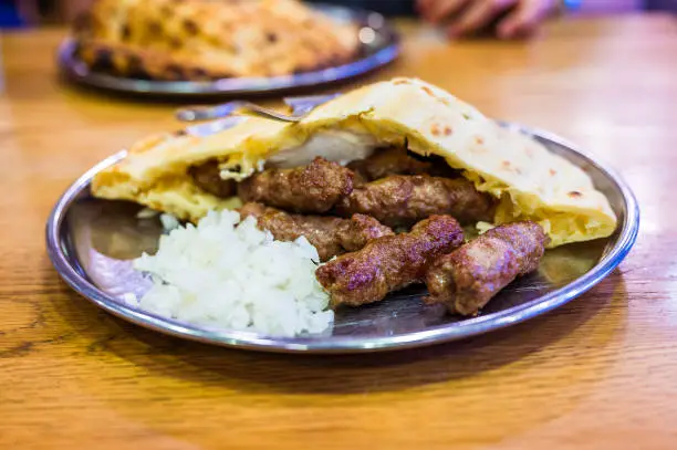 Traditional bosnian barbecue dish cevapi served with somun and chopped onions. Famous balkan BBQ dish served on an inox plate in Bascarsija, Sarajevo, Bosnia and Herzegovina.