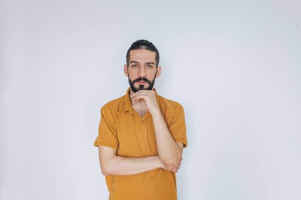 Middle age man wearing red t-shirt over white wall looking confident at the camera with smile with crossed arms and hand raised on chin. Thinking positive.