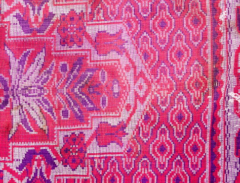 An attractive vintage wallpaper showcases a carpet pattern with a bright pink ornament against a backdrop of a vibrant red rug
