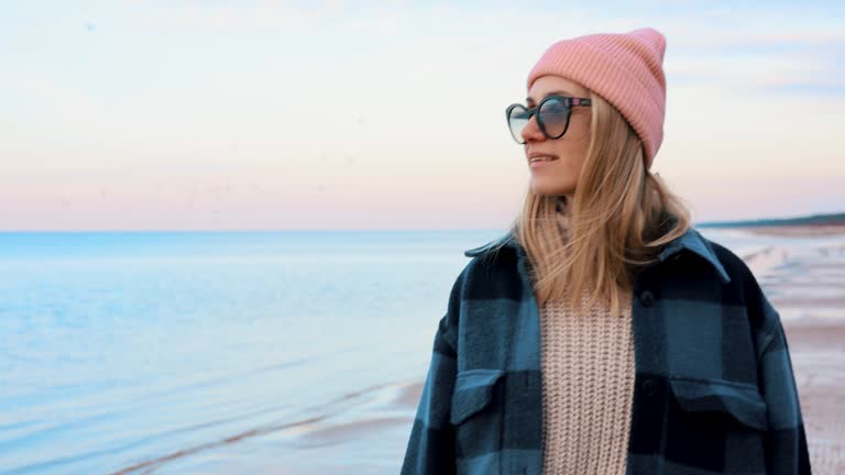 fashionable woman in coat and beanie hat enjoying walk on beach on chilly spring day