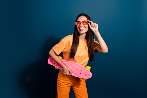 Photo of woman touching orange sunglasses had hobby ride skateboard looking empty space activities isolated on dark blue color background.