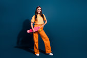 Full body length photo of young brunette woman holding her pink new longboard posing with purchase isolated on dark blue color background