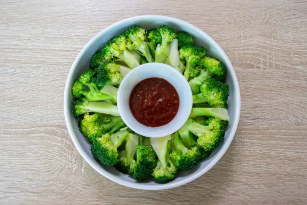 Blanched broccoli and vinegared red chili pepper paste on wood texture background.
