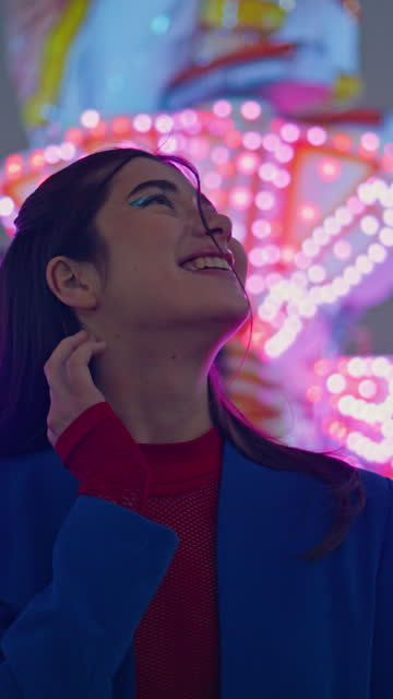 Happy girl enjoying amusement park at night vertically. Cheerful model at neon