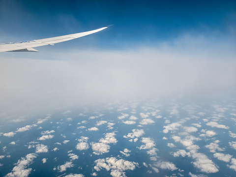 Cloud patterns with airplane flying between layers. Features plane wingtip and reflection. View through the cabin window.