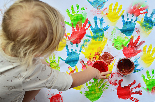 Child paints in nursey school on white background and making multi colured handprint.