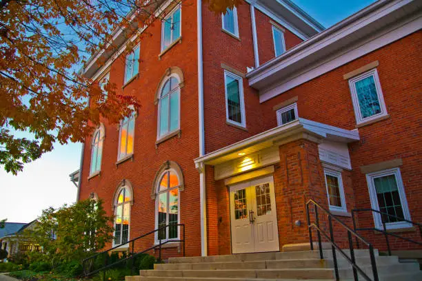 Captivating golden-hour view of a historic brick building in Fort Wayne, Indiana, surrounded by autumn foliage. Perfect for educational, institutional, or community-themed projects.