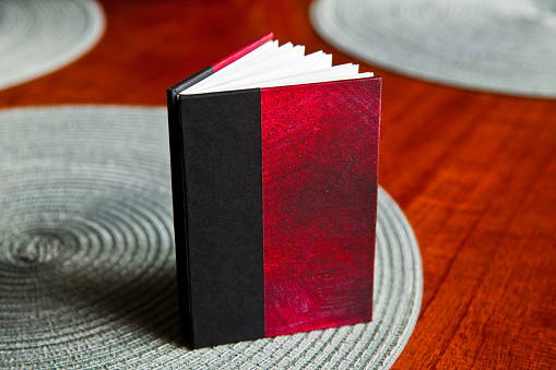 Striking black and red hardcover book on a polished wooden surface, inviting readers with its closed pages. Perfect for themes of literature, learning, and intellectual pursuits.