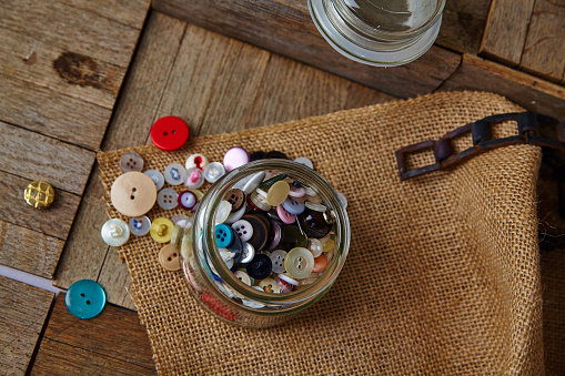 Craftsmanship in a Jar: A vibrant collection of buttons, showcasing diverse colors and designs, rests on a rustic burlap background.