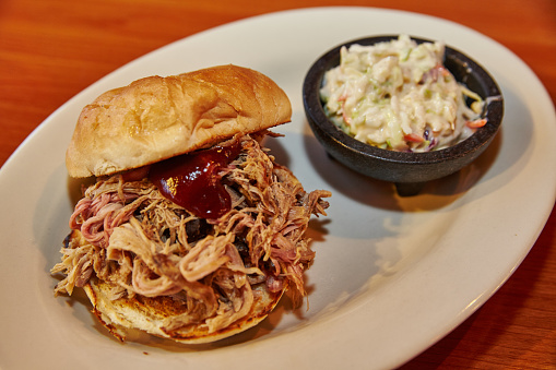 A mouthwatering pulled pork sandwich with a side of vibrant coleslaw, served on a wooden table in a cozy eatery. Perfect comfort food for any occasion.