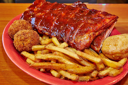 Indulge in a mouth-watering BBQ feast with glazed pork ribs, golden fries, and fried sides, served on a vibrant red plate. Perfect for showcasing American comfort food at its best. Culinary photography from Fort Wayne, Indiana.